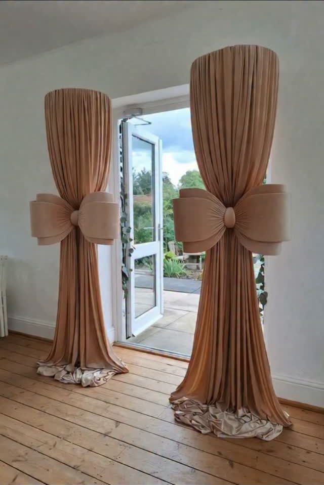 Two beige fabric drapes cinched with large bows flanking an open glass door.
