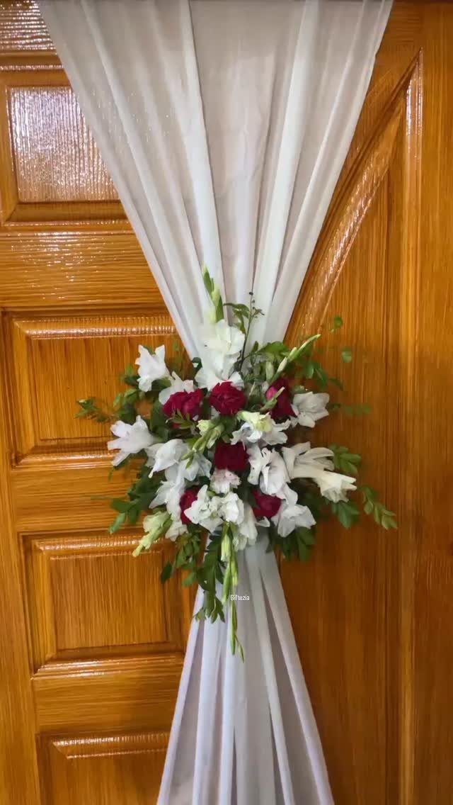 11 Wedding Decor Room Ideas for Your Reception in 2026 8 White sheer fabric draped over a wooden door, cinched with a red and white floral arrangement.