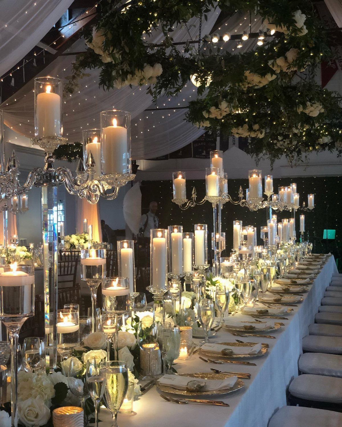 11 Wedding Decor Room Ideas for Your Reception in 2026 2 A long wedding reception table decorated with many white candles, silver candelabras, and white flowers.