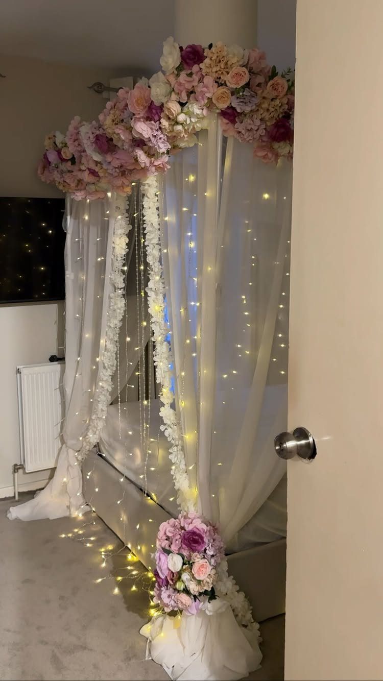 11 Wedding Decor Room Ideas for Your Reception in 2026 9 A bed decorated with white sheer fabric, pink floral arrangements, and twinkling fairy lights.