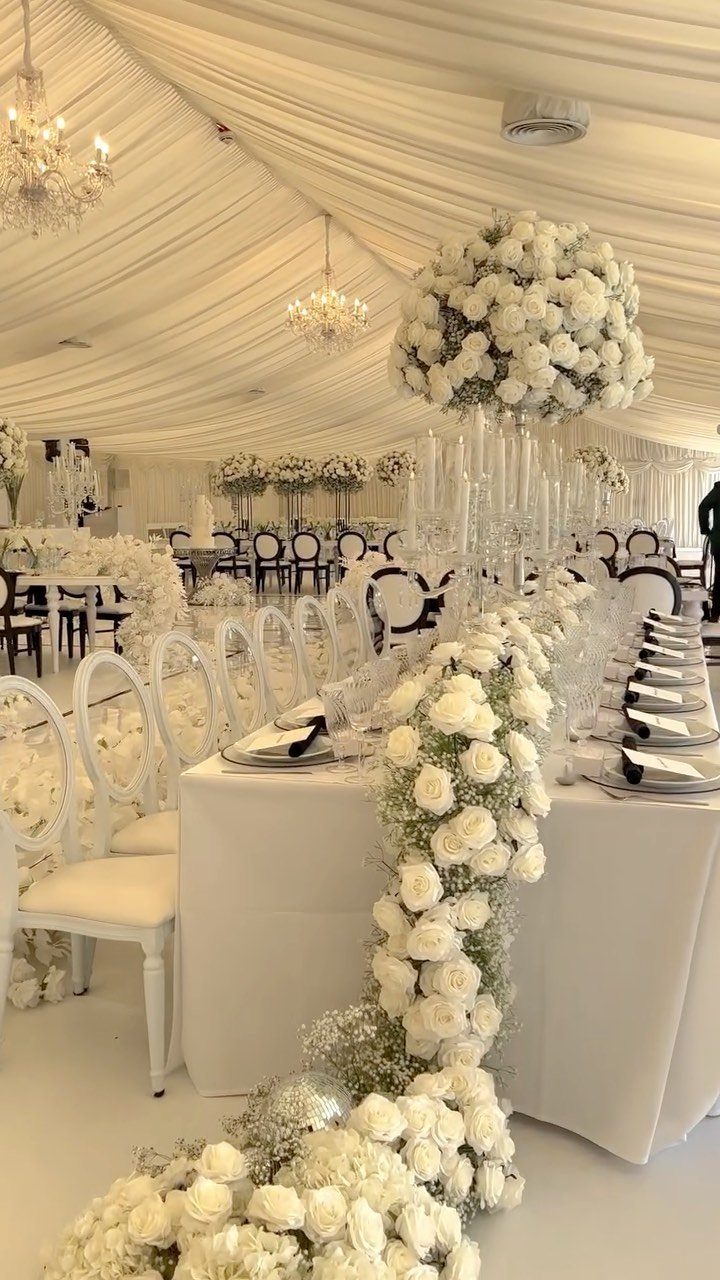 13 Wedding Decor Tent Ideas for 2026 Receptions 12 White wedding reception table decorated with rose garlands and crystal centerpieces inside a draped tent.