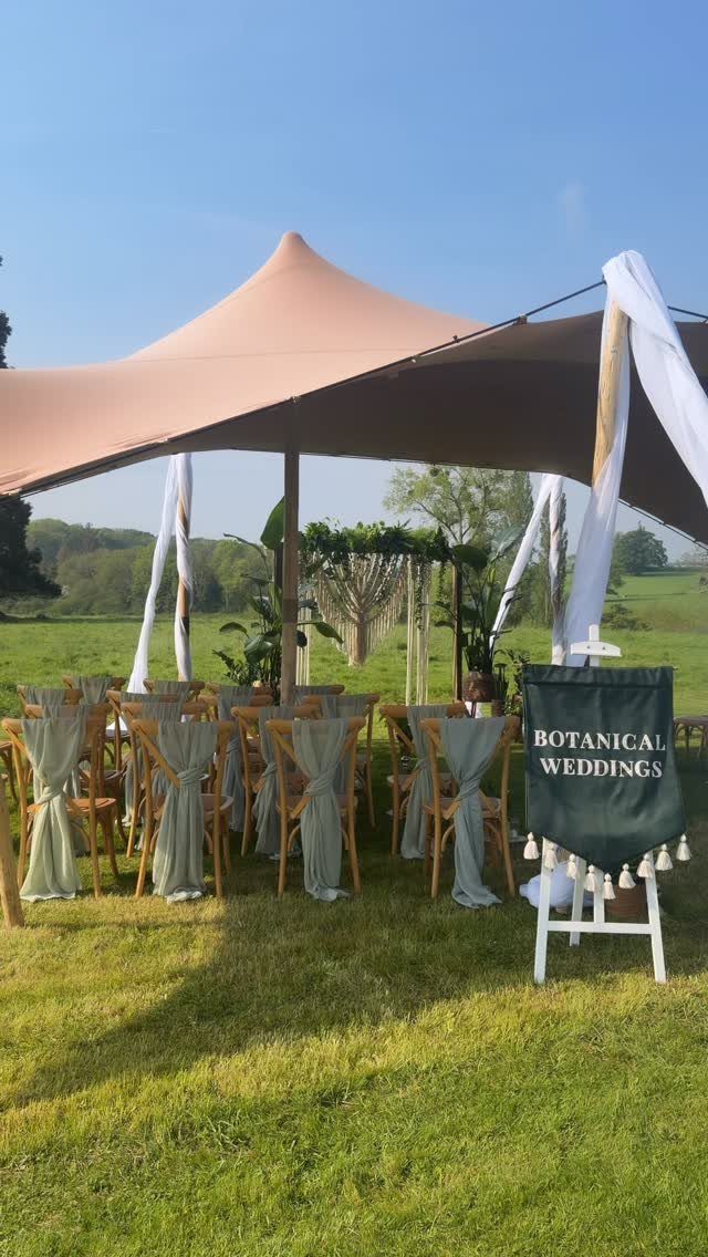 13 Wedding Decor Tent Ideas for 2026 Receptions 9 A tan sailcloth tent with draped white fabric and decorated wooden chairs on a green lawn.