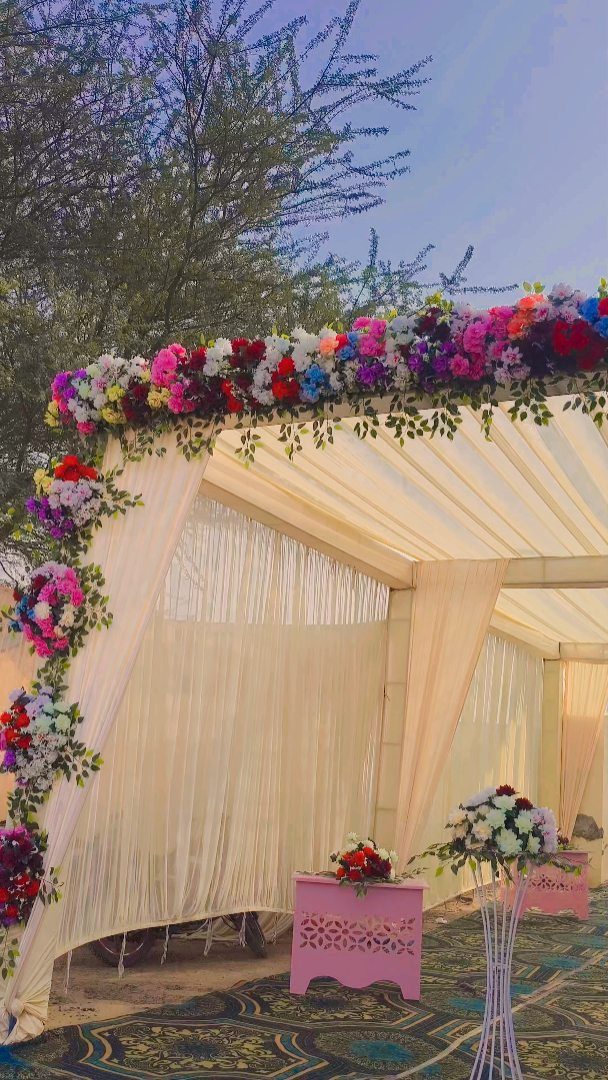 13 Wedding Decor Tent Ideas for 2026 Receptions 11 A cream fabric wedding tent decorated with a colorful floral garland and draped fabric outdoors.
