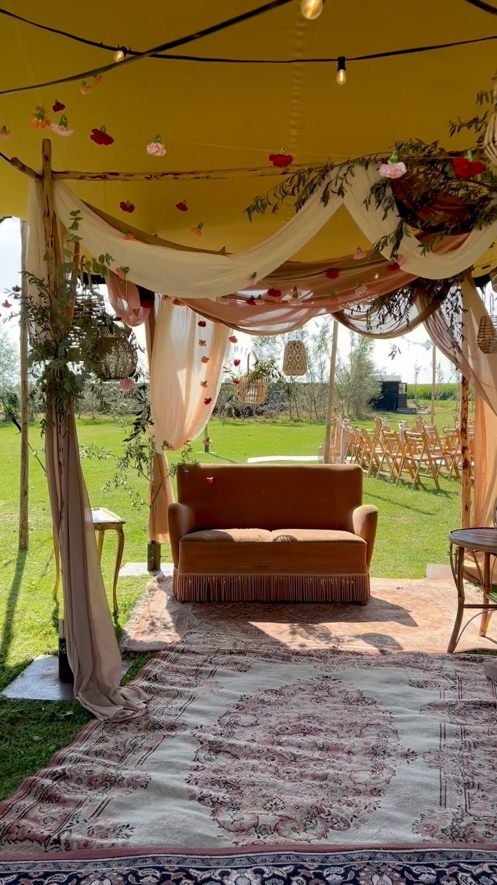 13 Wedding Decor Tent Ideas for 2026 Receptions 7 A rustic bohemian wedding lounge with a velvet sofa, draped fabric, and patterned rugs under a tent.