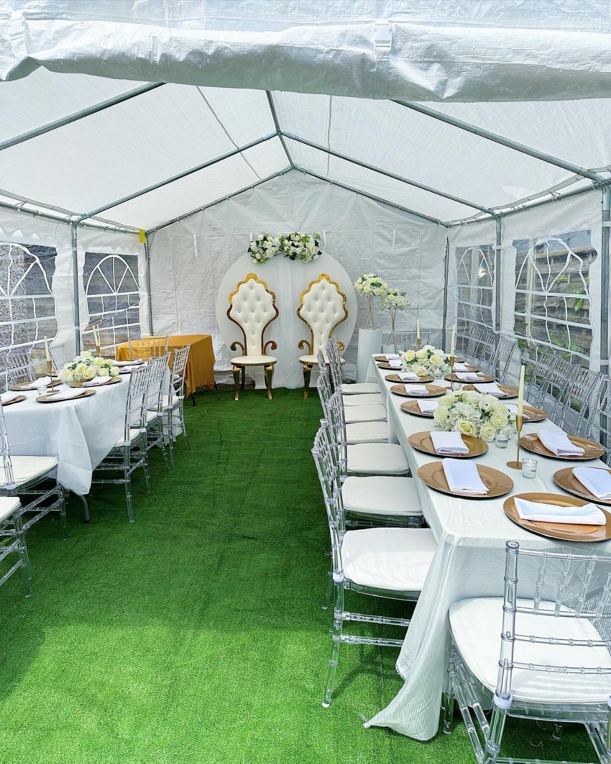 13 Wedding Decor Tent Ideas for 2026 Receptions 2 White dining tables with floral centerpieces and gold chargers inside a clear wedding tent.