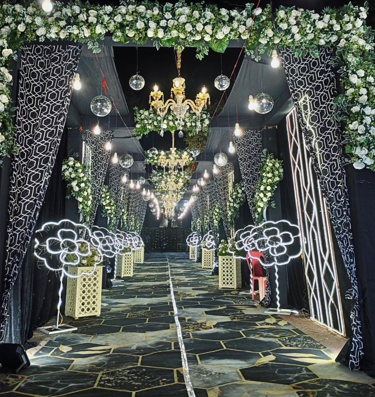 13 Wedding Decor Tent Ideas for 2026 Receptions 6 A decorated wedding tent entrance with patterned drapes, floral garlands, chandeliers, and geometric patterned flooring.