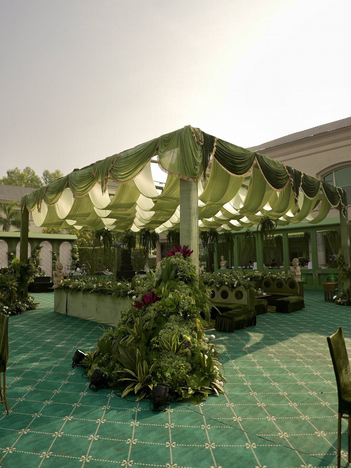 Wedding Decor and Themes: 12 Ideas From Beach to Garden 11 A large green outdoor canopy decorated with white fabric swags and lush greenery on a patterned carpet.