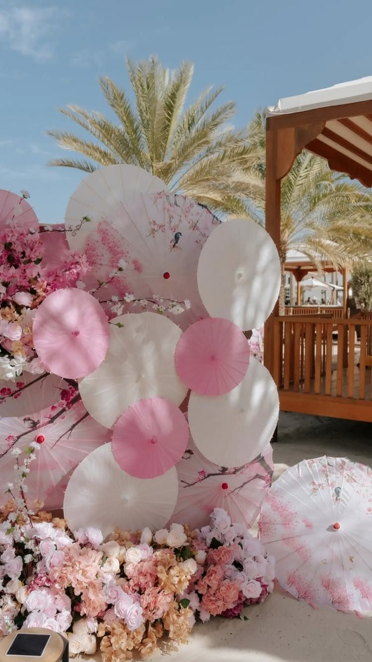 Wedding Decor and Themes: 12 Ideas From Beach to Garden 12 Pink and white paper parasols arranged with flowers near palm trees under a blue sky.