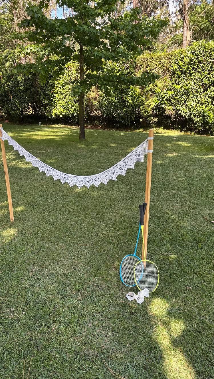 A lace badminton net set up on a sunny green lawn with rackets and a shuttlecock.