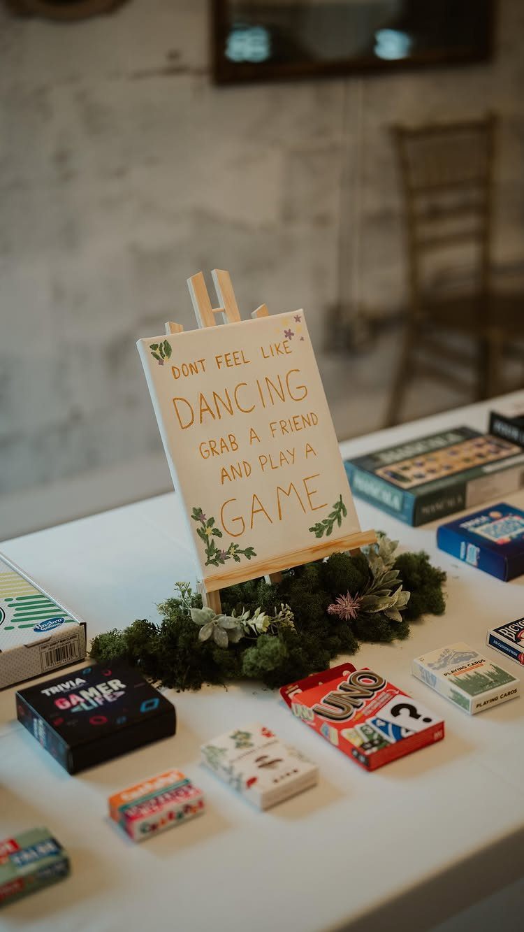 Various board games and card games arranged on a table next to a small sign on an easel.
