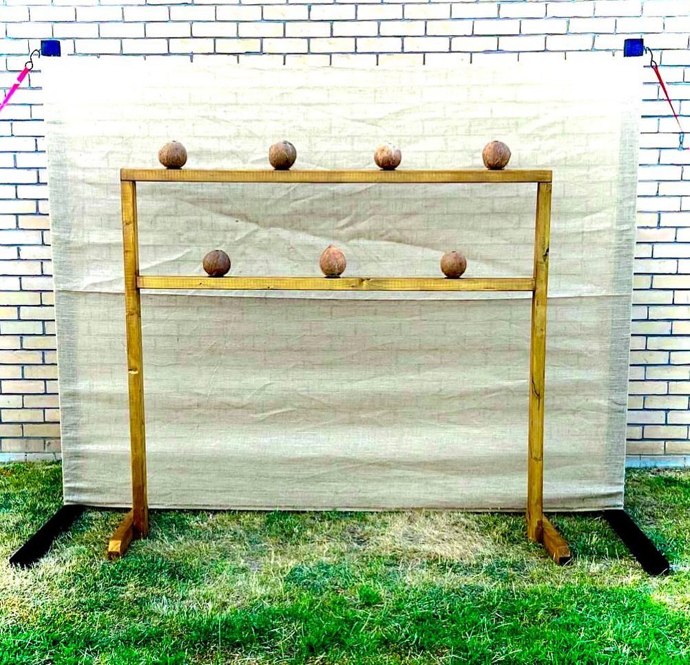 A wooden coconut shy game setup with coconuts on bars against a canvas backdrop.