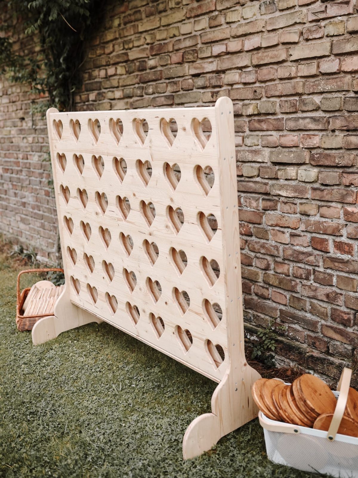 Large wooden heart-shaped cutout game board standing on grass against a brick wall.