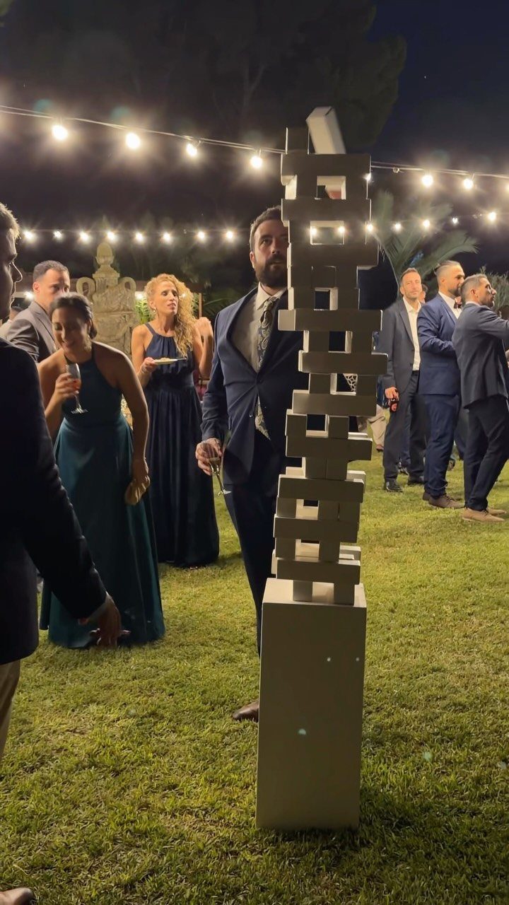 A man in a suit carefully playing giant Jenga with large white blocks outdoors at night.
