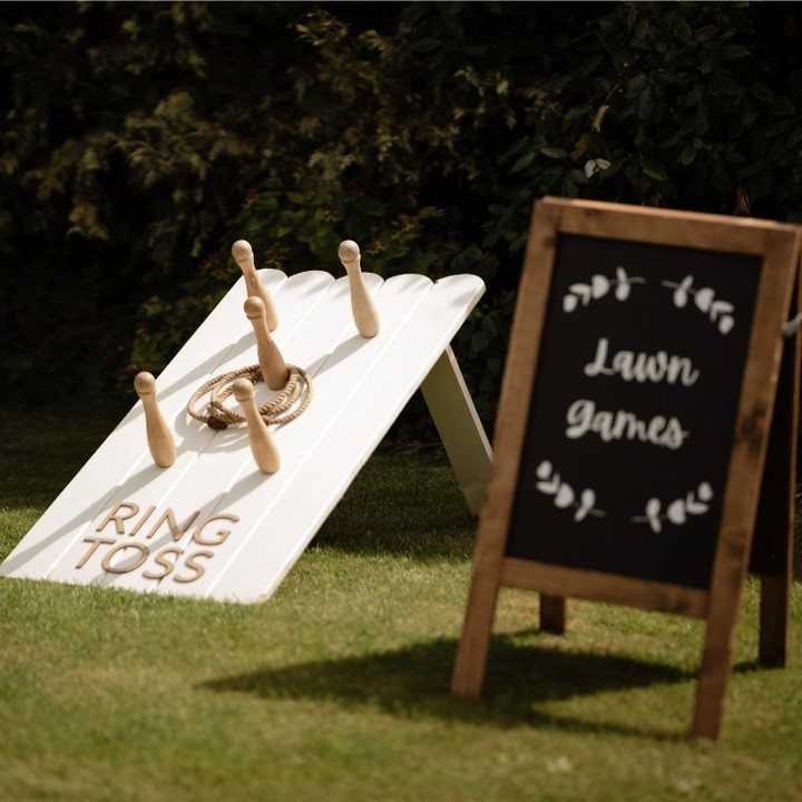 Wooden ring toss game set on a white slanted board with a lawn games chalkboard sign.