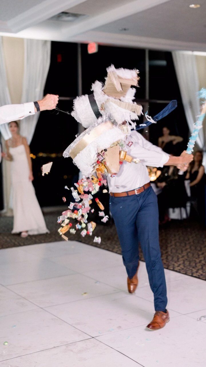 A man hitting a white piñata as colorful candies spill out during a wedding reception.