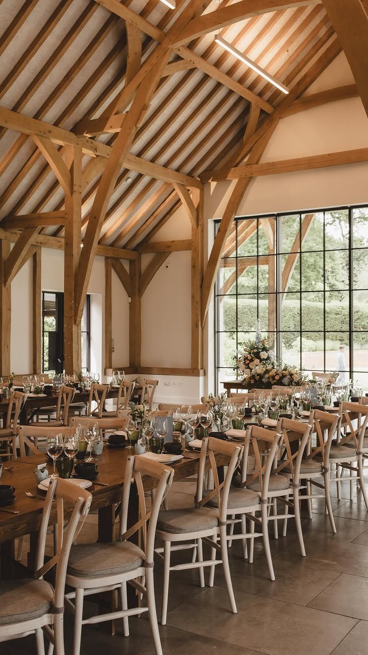 A wedding reception setup inside a rustic barn with exposed wooden beams and large windows.