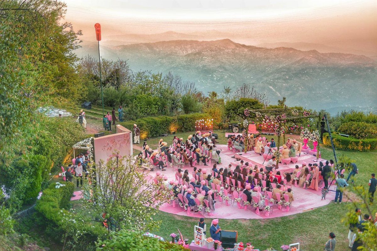 An outdoor wedding ceremony with pink chairs set against a scenic mountain range at sunset.