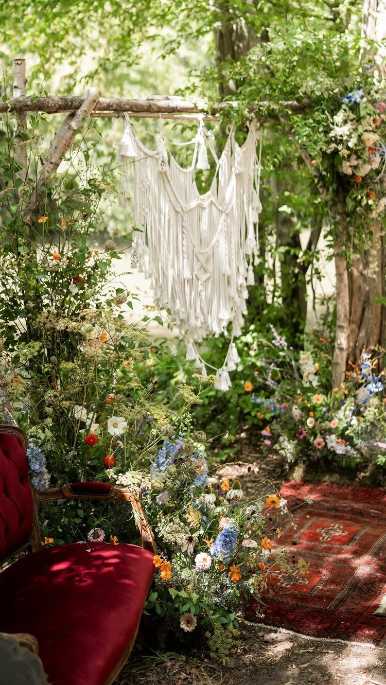 A rustic wooden arch with white macrame and wildflowers in a sunlit forest setting.