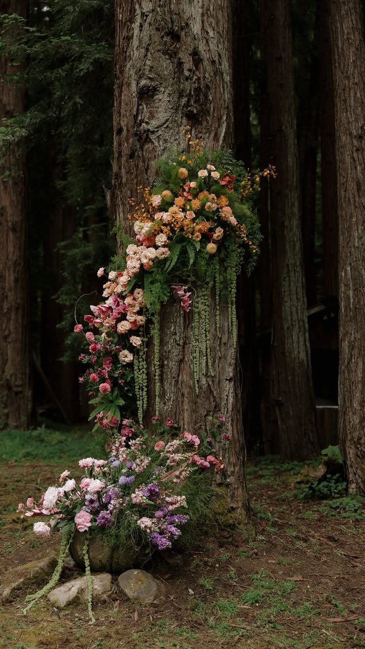 Colorful flowers cascading down a large tree trunk in a dark forest setting.