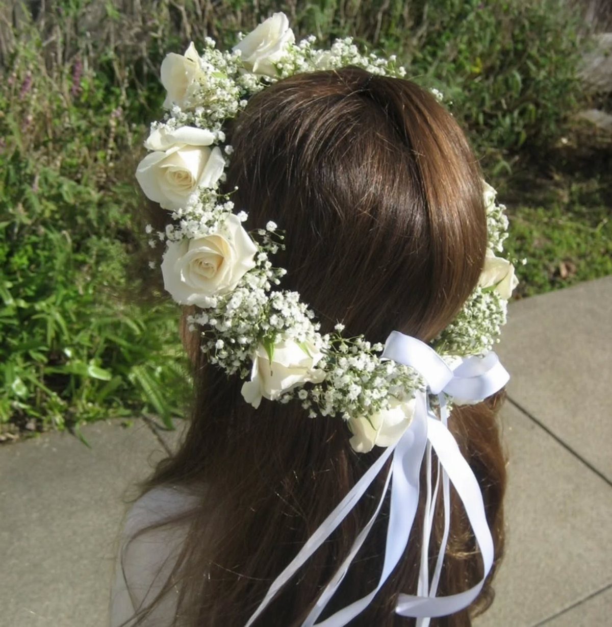 A person wearing a delicate floral crown of white roses and baby's breath with a white ribbon.
