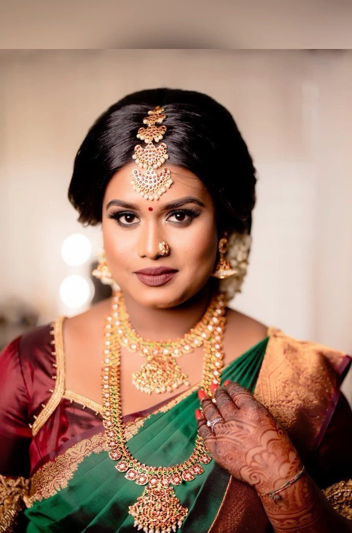 A South Asian bride wearing traditional gold jewelry and a green silk saree.