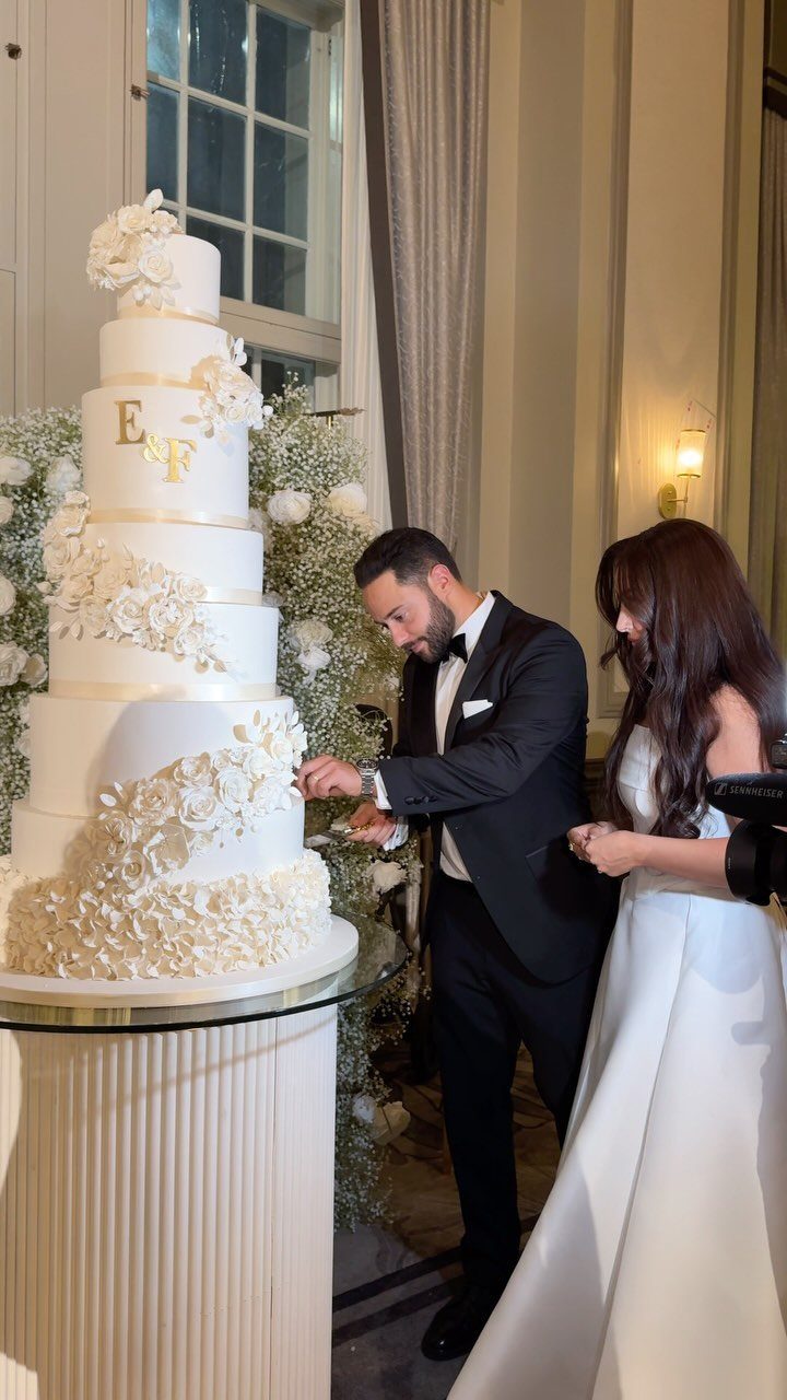 A bride and groom standing next to a large, tiered white floral wedding cake.