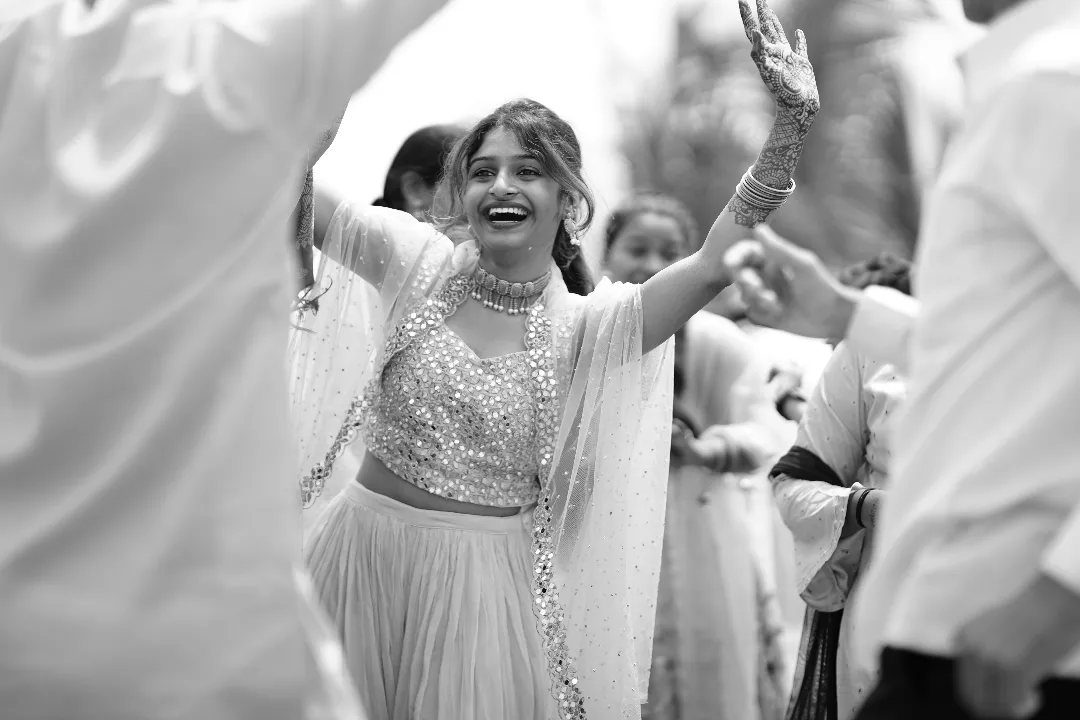 A smiling woman in traditional Indian clothing dancing with her arms raised during a celebration.