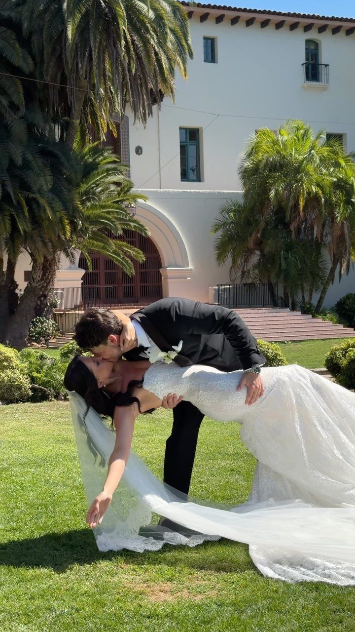 A groom dips his bride for a kiss on a sunny lawn in front of a villa.