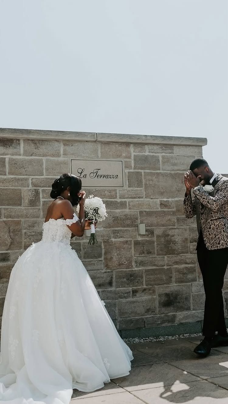 A bride and groom preparing for their first look moment in front of a stone wall.