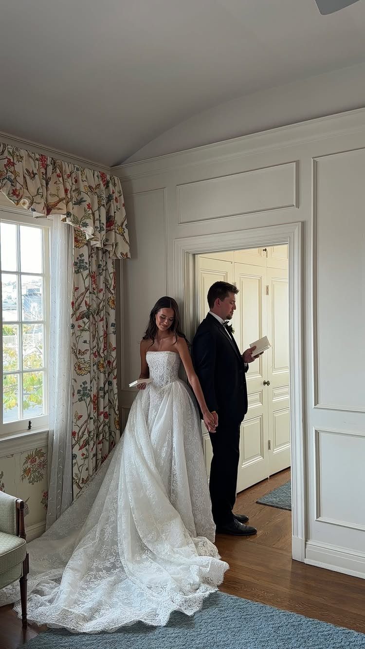 Bride and groom standing back-to-back holding hands through a doorway in a white room.