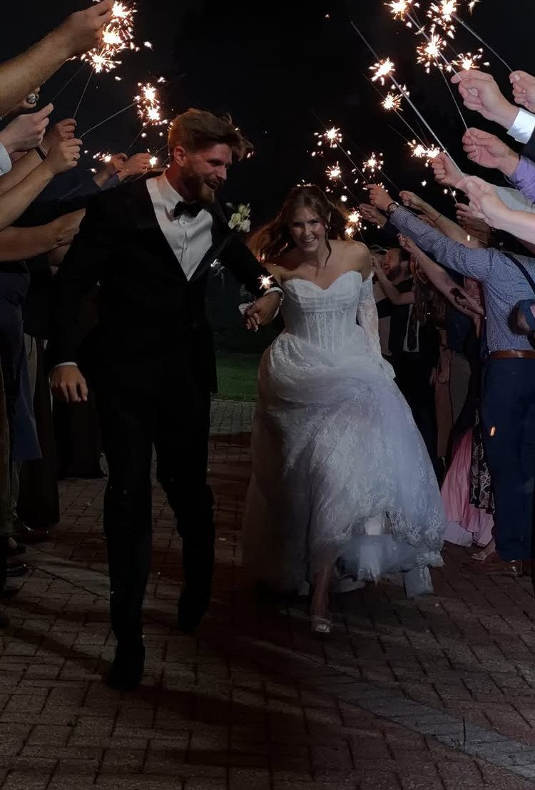 A bride and groom walking through a celebratory sparkler exit held by wedding guests at night.