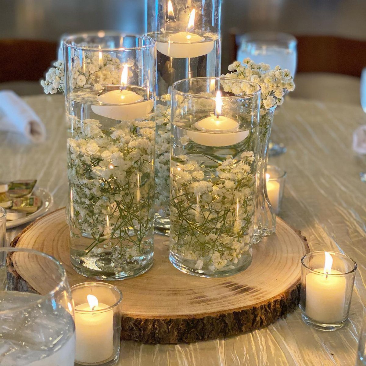 11 Wedding Party Table Decor Ideas for Any Venue Style 8 Tall glass cylinders with floating candles and white baby's breath flowers on a wooden base.