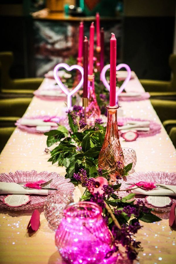 11 Wedding Party Table Decor Ideas for Any Venue Style 10 A decorated wedding table featuring pink candles, greenery, and glowing pink heart-shaped neon signs.