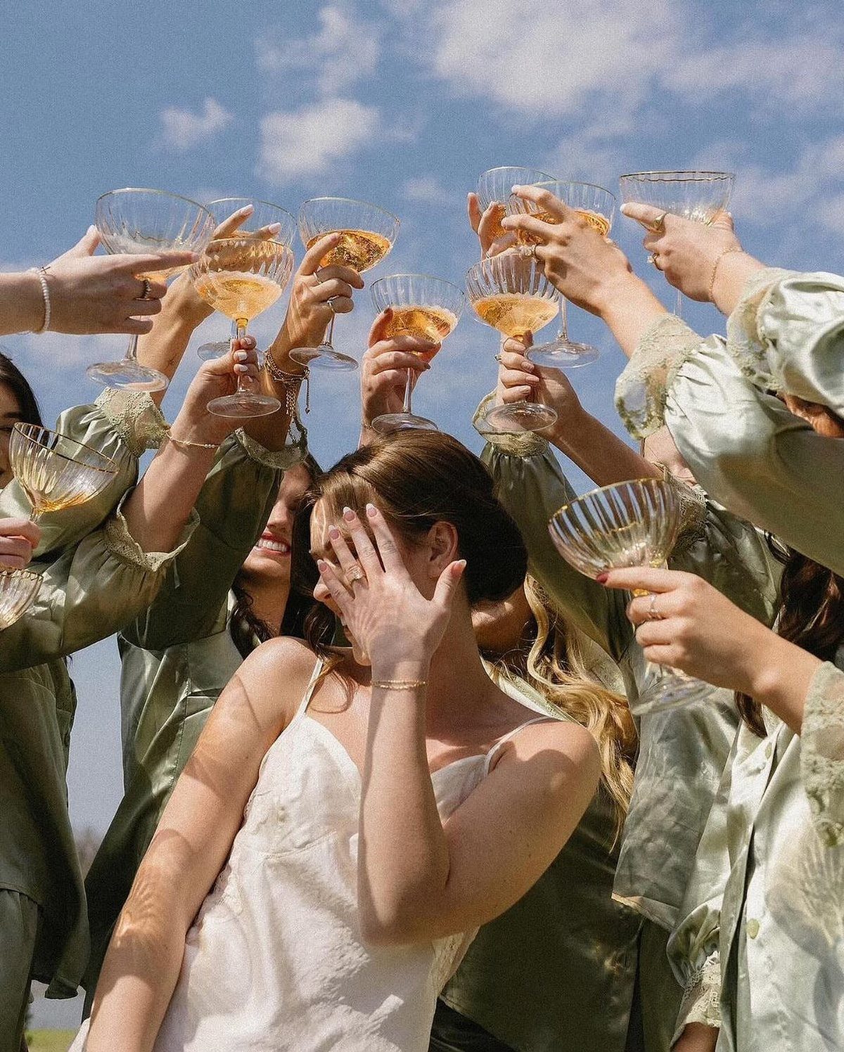 13 Wedding Photo Ideas for Your Shot List 11 Women in satin robes raising champagne glasses in a toast under a blue sky.