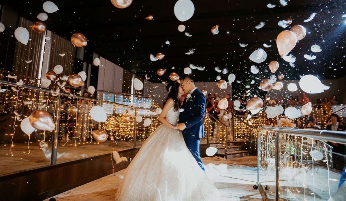 13 Wedding Photo Ideas for Your Shot List 10 A bride and groom embrace while white and rose gold balloons fall around them.