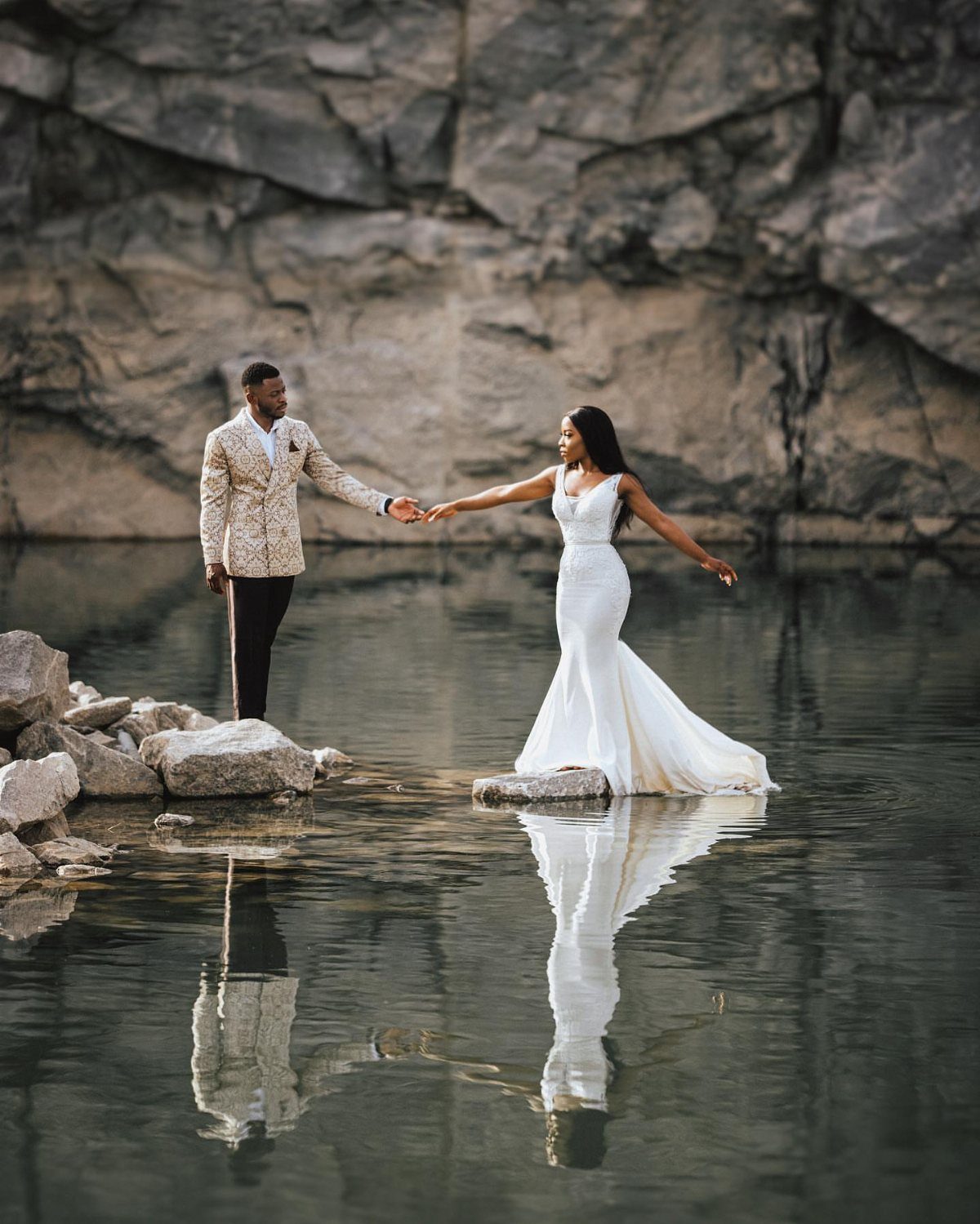 13 Wedding Photo Ideas for Your Shot List 1 A bride and groom holding hands by a lake with their reflections visible in the water.