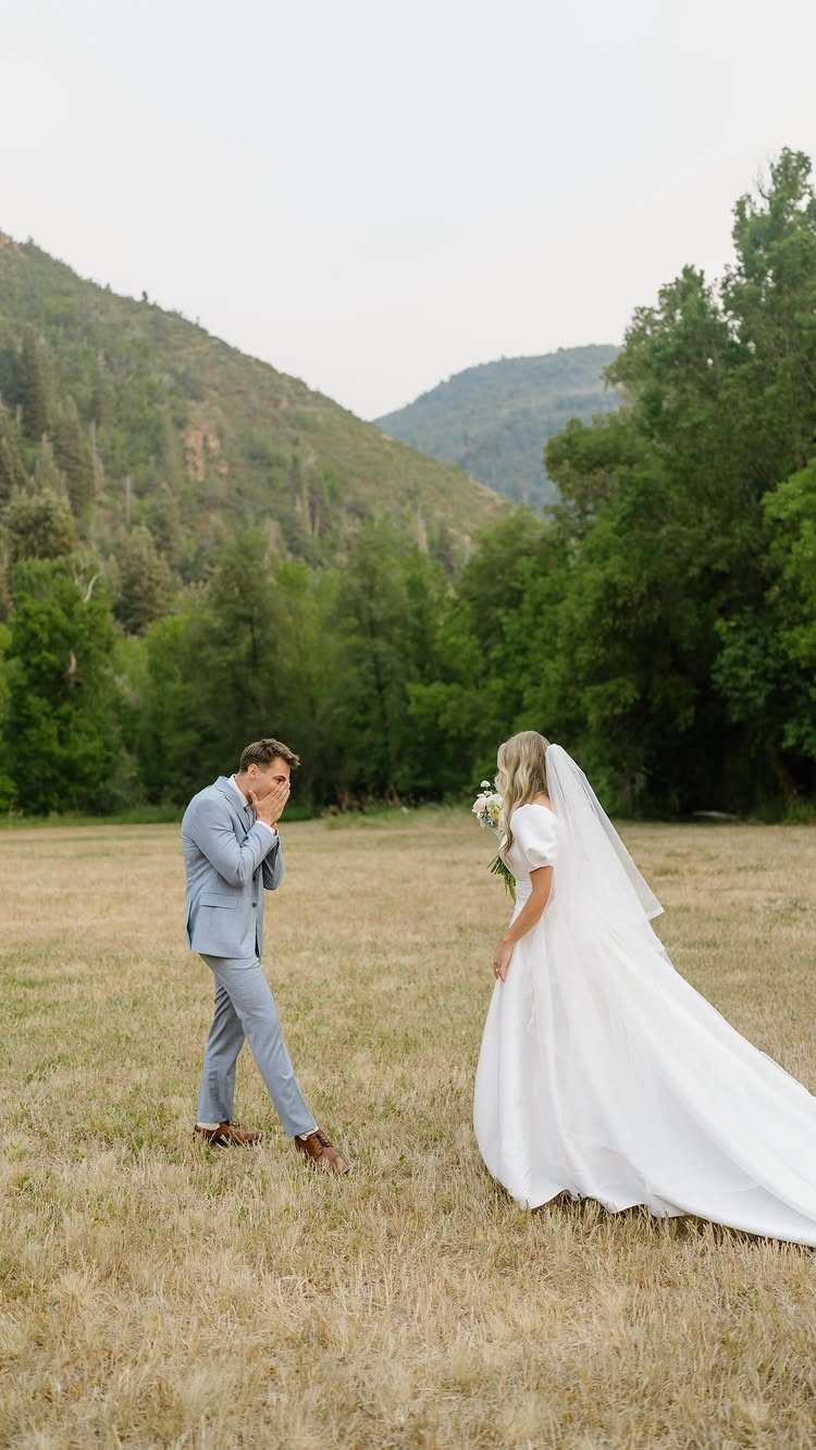 9 Wedding Photos Poses for Every Part of Your Day 2 A groom reacts with surprise as a bride approaches him in a grassy mountain field.