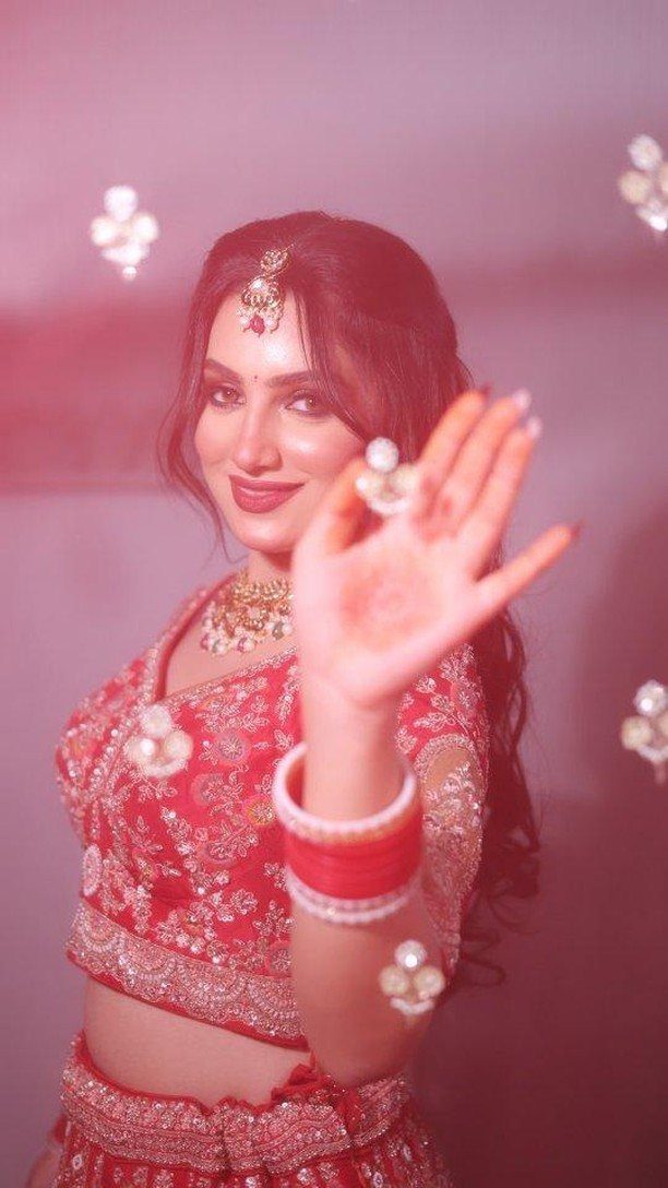 9 Wedding Photos Poses for Every Part of Your Day 5 A smiling bride in red traditional Indian clothing posing with her hand near the camera.