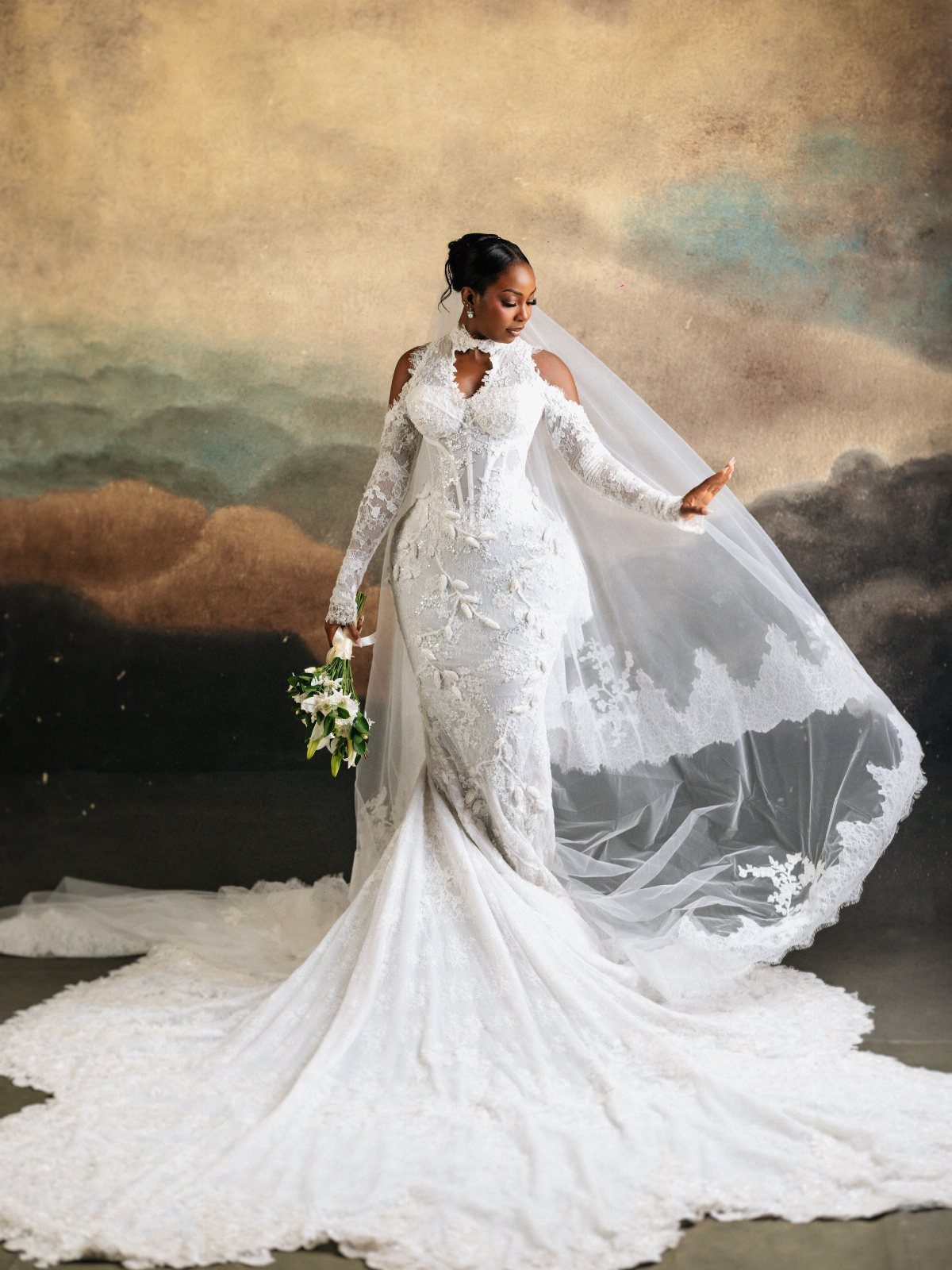 9 Wedding Photos Poses for Every Part of Your Day 4 A bride in a lace gown holds her veil out against a scenic backdrop.