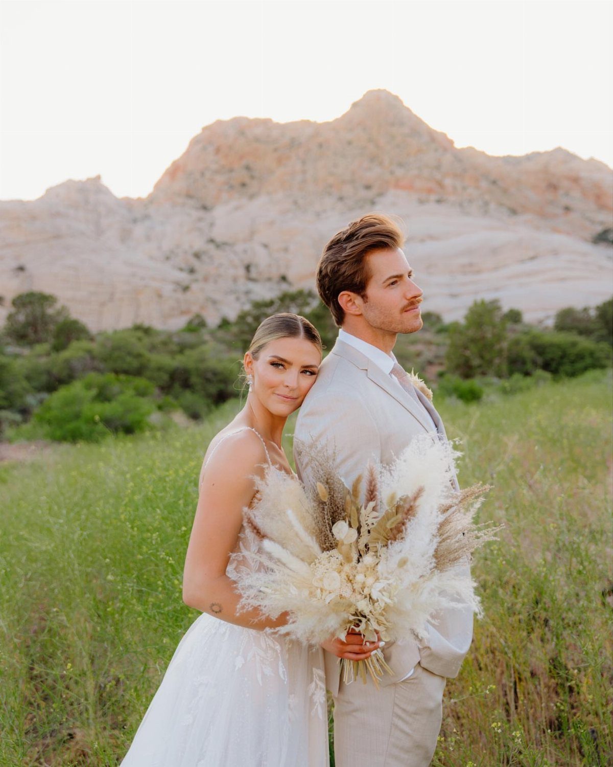 9 Wedding Photos Poses for Every Part of Your Day 6 A bride leaning her head on the groom's back while holding a large dried floral bouquet outdoors.