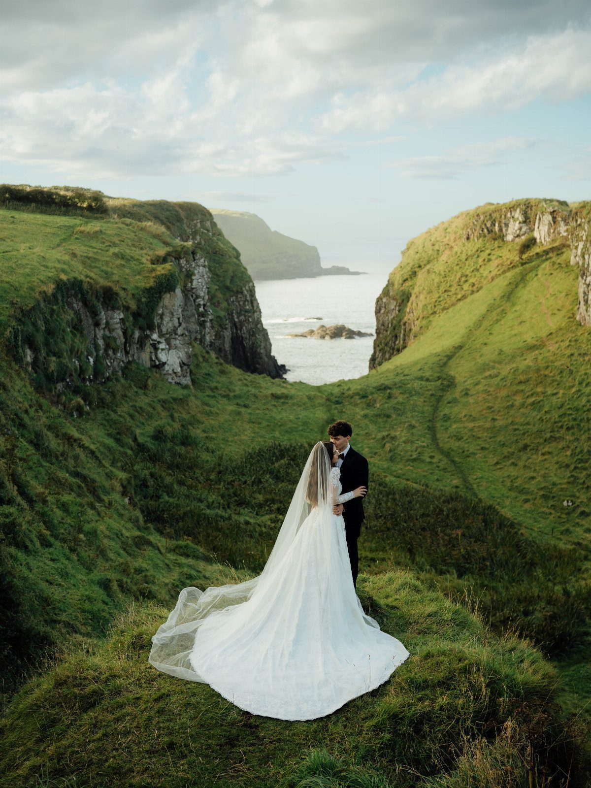 9 Wedding Photos Poses for Every Part of Your Day 8 A bride and groom standing on a grassy cliff overlooking the ocean waves.