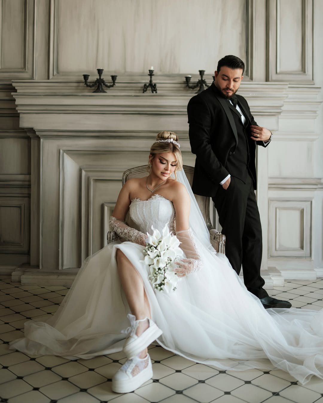9 Wedding Photos Poses for Every Part of Your Day 7 A bride in a white wedding dress and sneakers sits with a bouquet next to a groom.