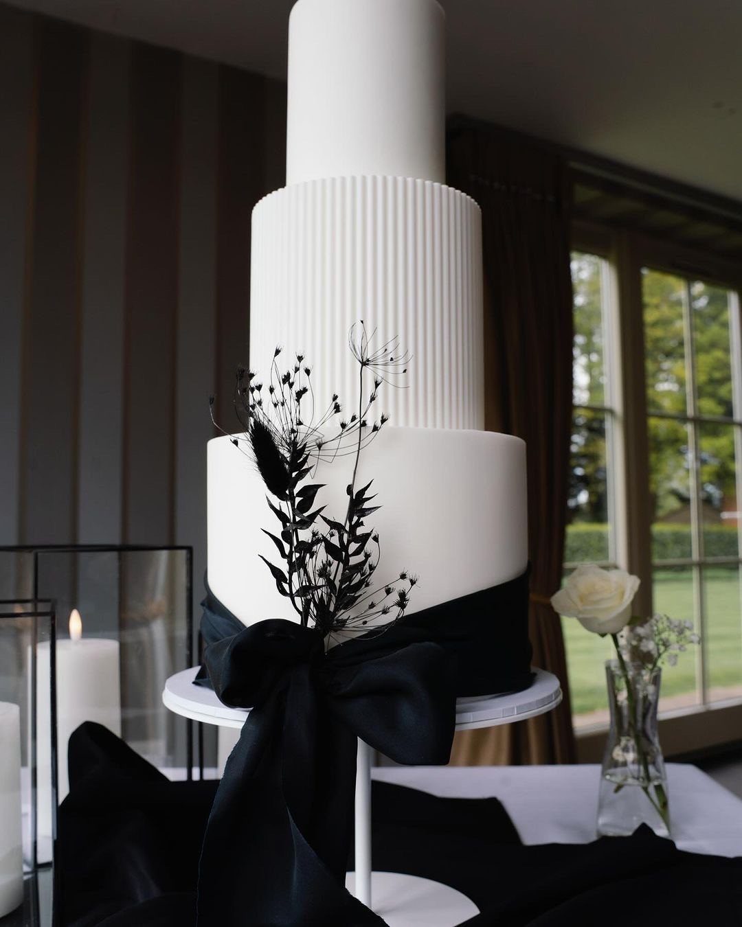 A three-tiered white wedding cake with black ribbon and black dried flowers.
