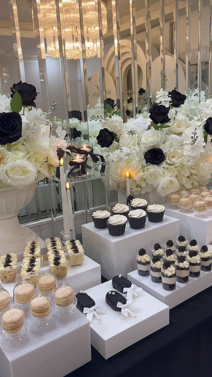 White and black floral arrangements and desserts arranged on a table with a mirrored background.