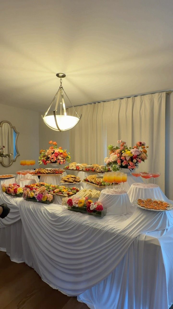 20 Spring Wedding Theme Ideas for 2026 18 A long buffet table laden with brunch foods and colorful floral arrangements under a hanging light.