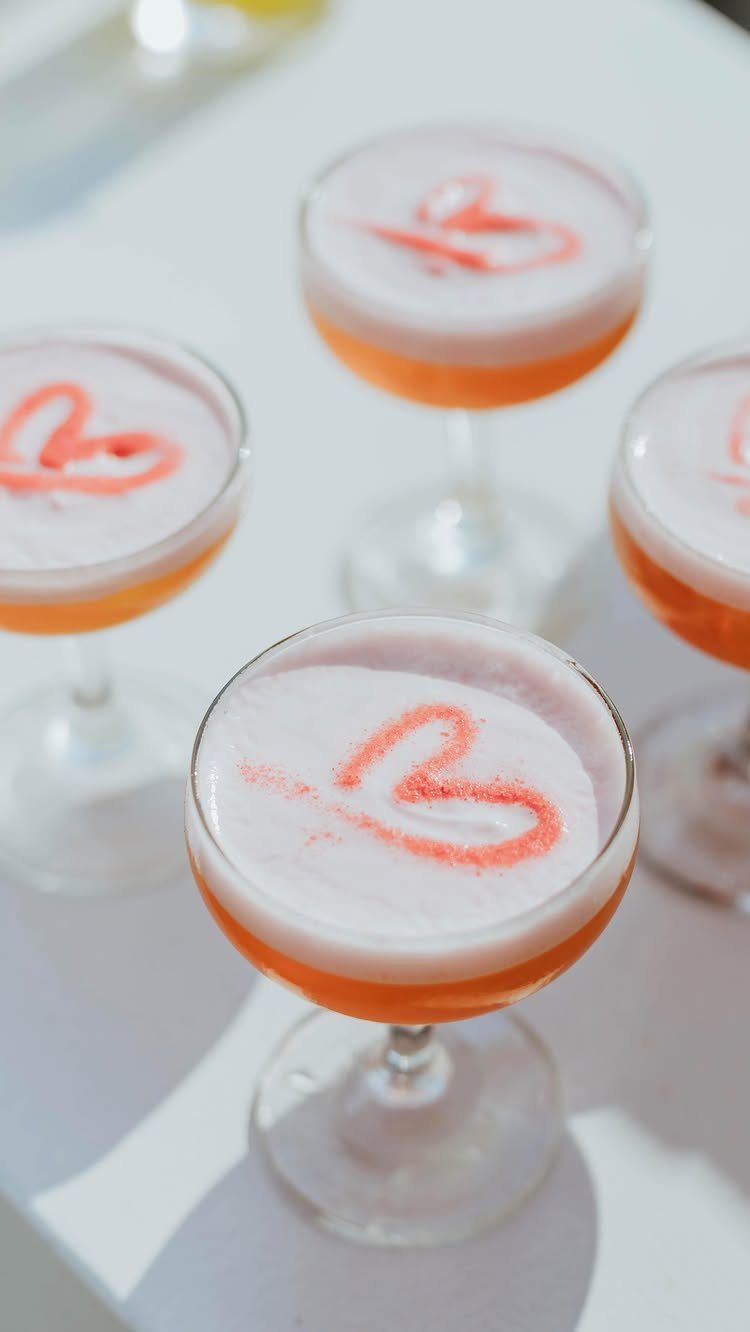 20 Spring Wedding Theme Ideas for 2026 12 Four orange cocktails with white foam and pink heart dustings in coupe glasses.