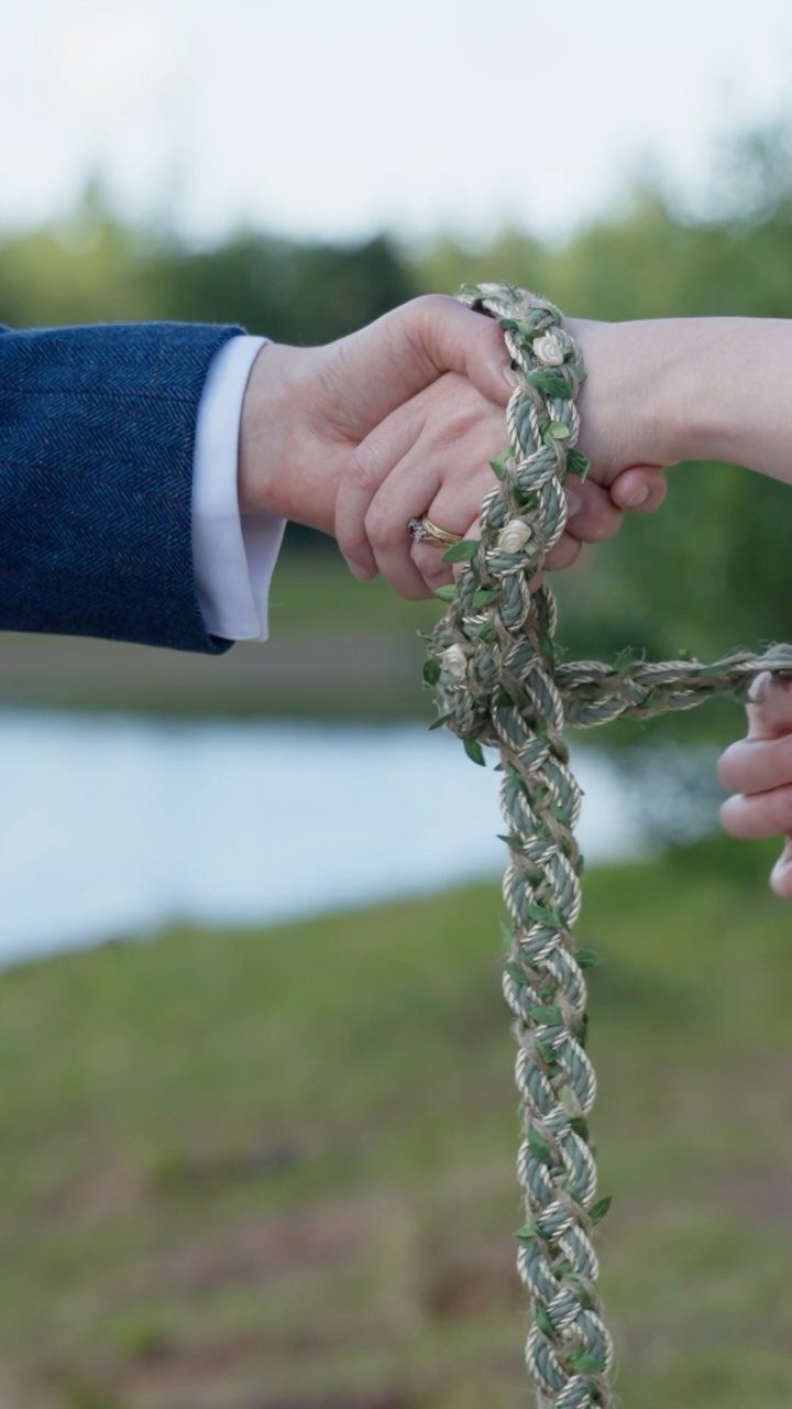 20 Spring Wedding Theme Ideas for 2026 17 Hands holding each other entwined by a braided floral rope in an outdoor setting.