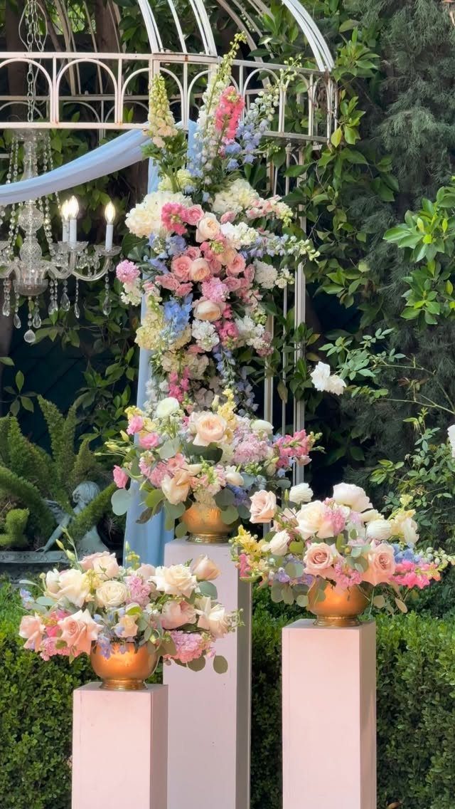 20 Spring Wedding Theme Ideas for 2026 1 Pastel pink and blue floral arrangements on pedestals under a white garden arch.