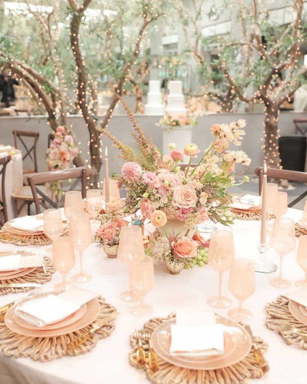 20 Spring Wedding Theme Ideas for 2026 6 Peach floral centerpieces and gold chargers on a wedding reception table with fairy lights.