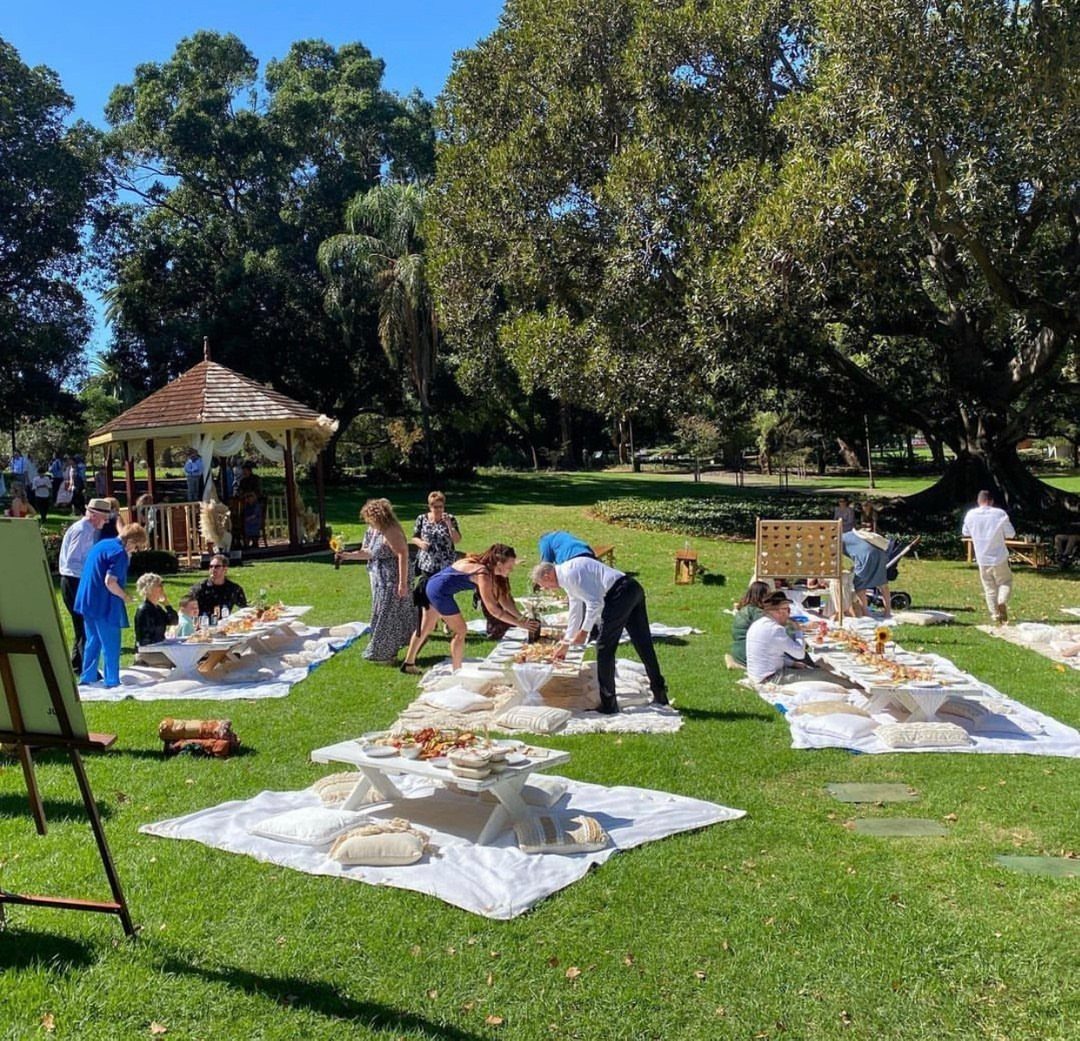 20 Spring Wedding Theme Ideas for 2026 11 People enjoying a picnic-style lounge area with low tables and blankets on a sunny lawn.